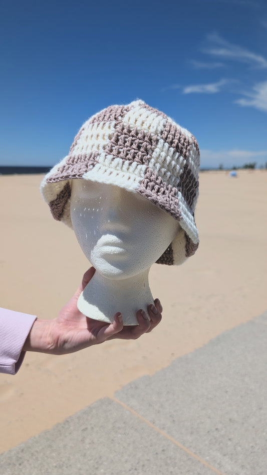 Mannequin head wearing a checkered sun hat with a beach in the background