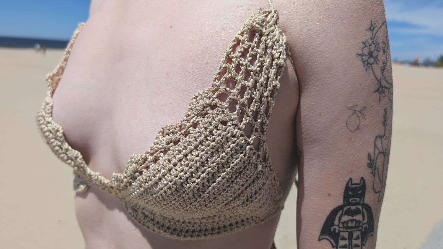 Person wearing a beige crochet bikini top on a beach with tattoos visible.