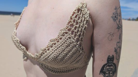 Person wearing a beige crochet bikini top on a beach with tattoos visible.