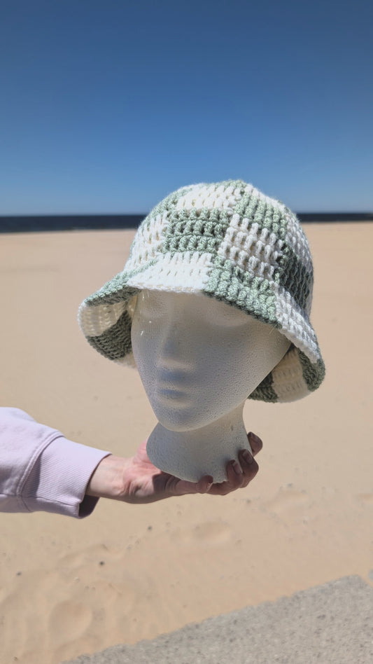 Mannequin head wearing a green and white textured sun hat on a sandy background