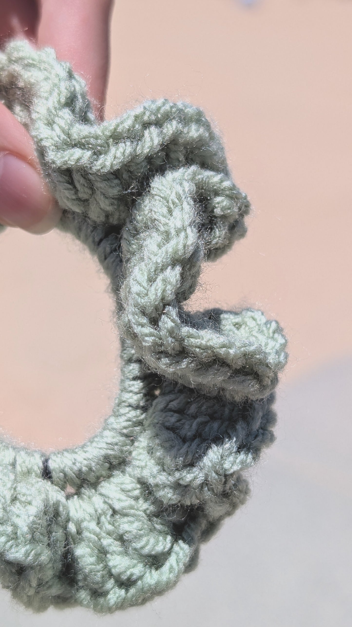Close-up of a textured green scrunchie held by a hand against a neutral background