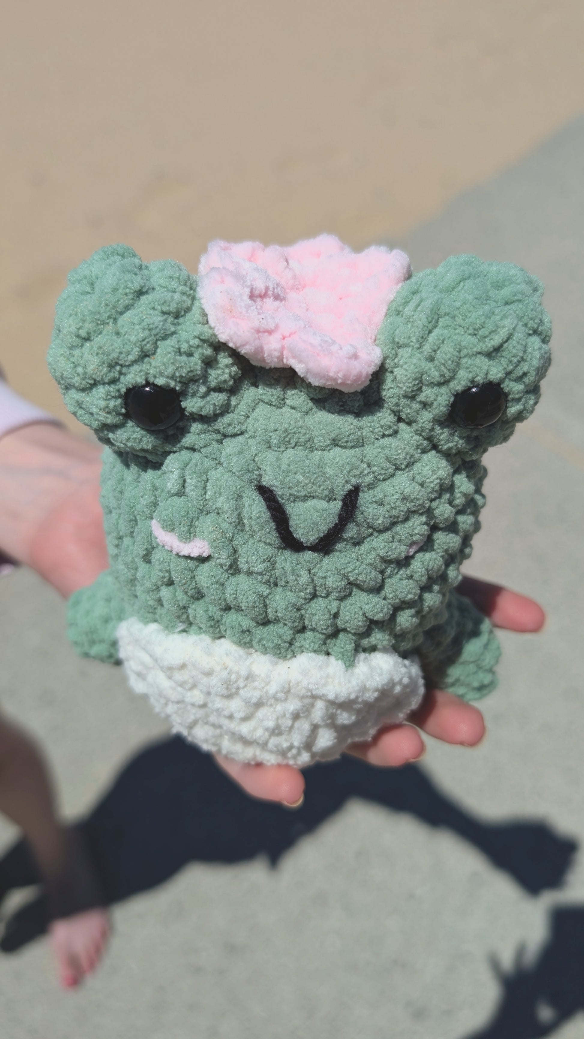 Green plush toy with a pink flower on a blurred background