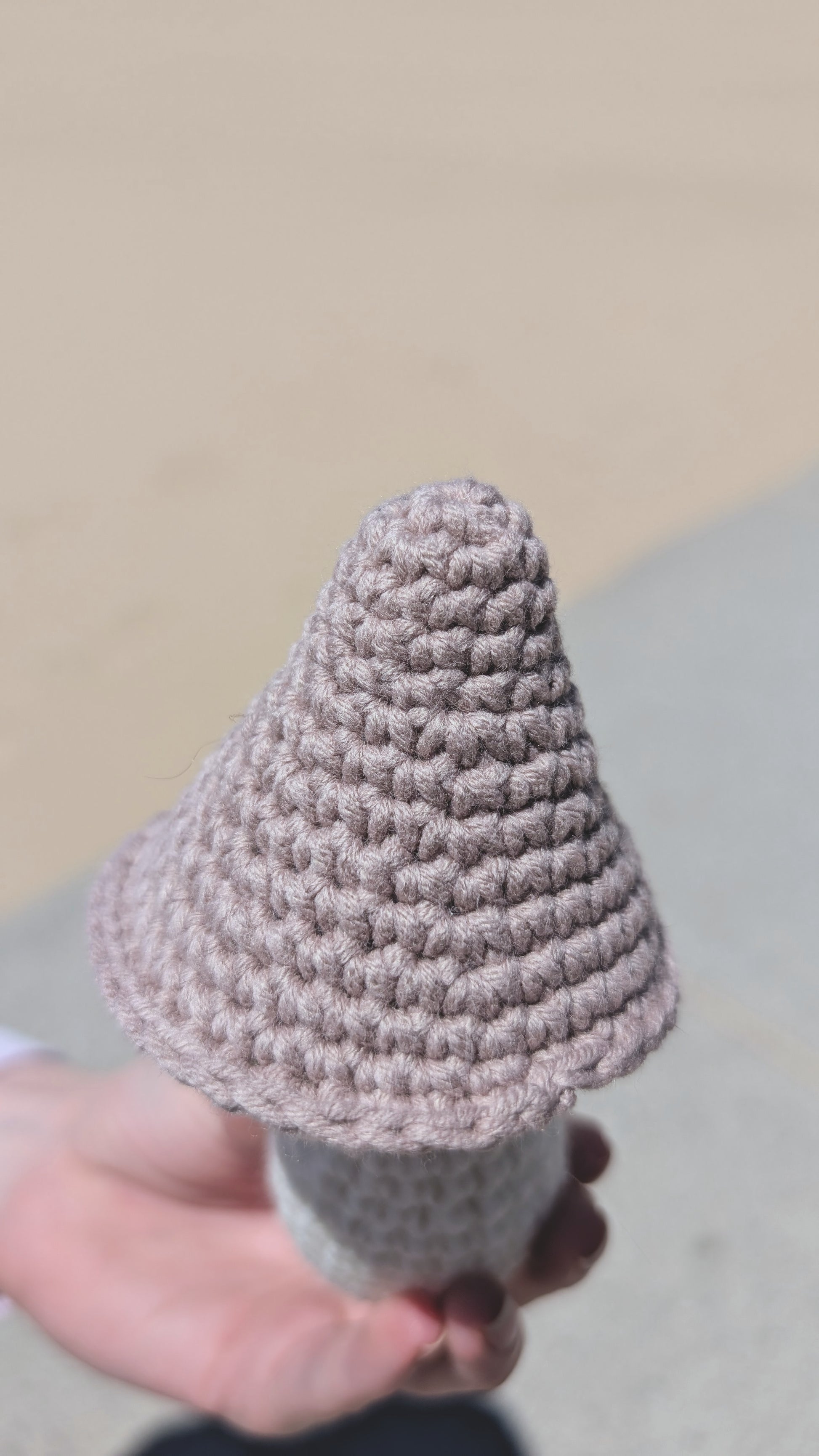 Hand holding a small crochet mushroom against a neutral background